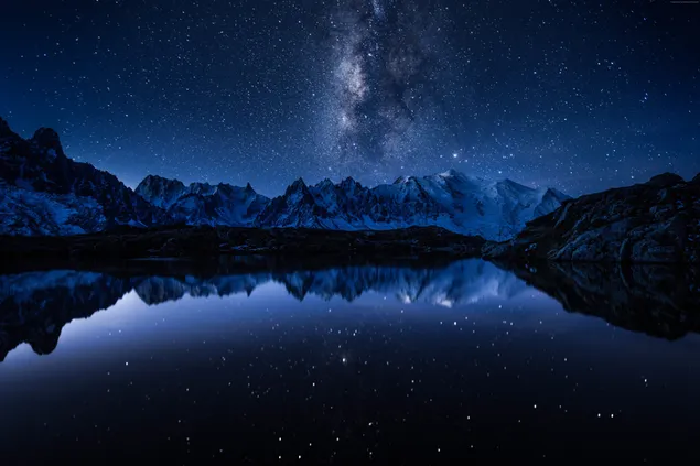 De weerspiegeling van de besneeuwde bergen in het water, verlicht door de stralende sterren in de pikdonkere nacht