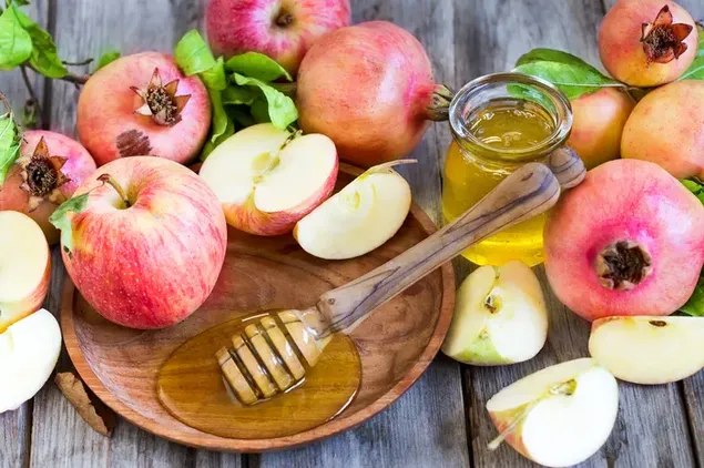 De zoetste appel en granaatappel van de natuur met een potje honing op een houten tafel