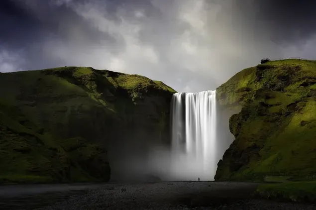 Der herrliche Blick auf den Wasserfall, der zwischen zwei Hügeln fließt und in die dunklen Wolken reicht