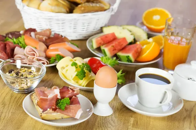 Desayuno saludable y abundante con pan, frutas, carne, huevo, café y jugo.