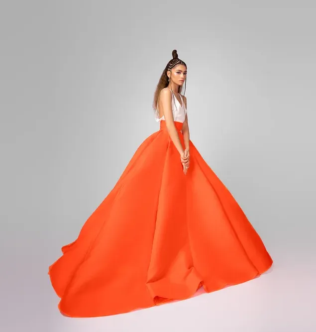Die junge amerikanische Schauspielerin Zendaya posiert mit ihrem langen orangefarbenen Rock und gerafften Haaren für die Kamera herunterladen