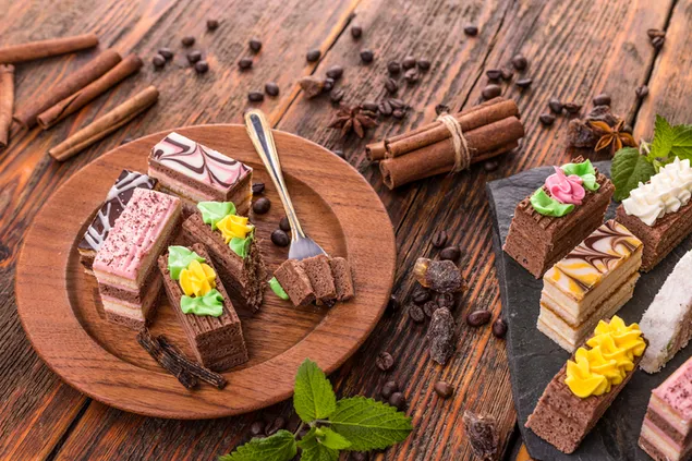 Diferentes sabores de pastel en rodajas en un plato de madera y una bandeja con palitos de canela y granos de café al lado