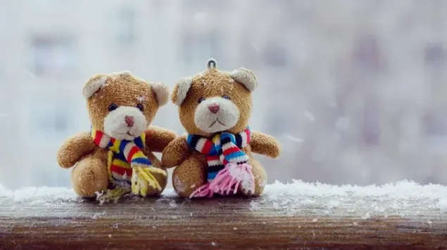 Dos encantadores osos de peluche con bufandas abrazándose sentados en el suelo de madera cubierto de nieve en invierno