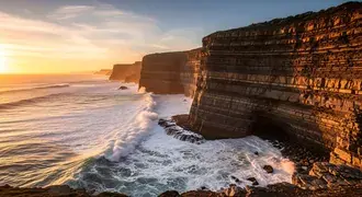dramatic sea cliffs glow in the golden light of sunset as waves crash below, creating a breathtaking coastal landscape with vivid patterns and texture download