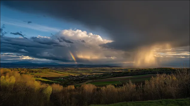 Dramateschen, stürmeschen Himmel mat engem Reebou iwwer enger grénger Landschaft 2K Tapeten