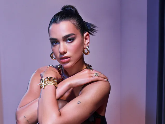 Dua lipa con las manos en los hombros, el cabello negro recogido hacia atrás, con sus joyas de oro. descargar