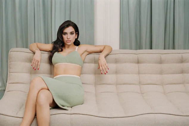 Dua lipa sentada en un sofá color crema con vestido verde, cortinas verdes al fondo HD fondo de pantalla