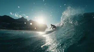 dynamic action shot of a surfer on a wave crest against bright sunlight.