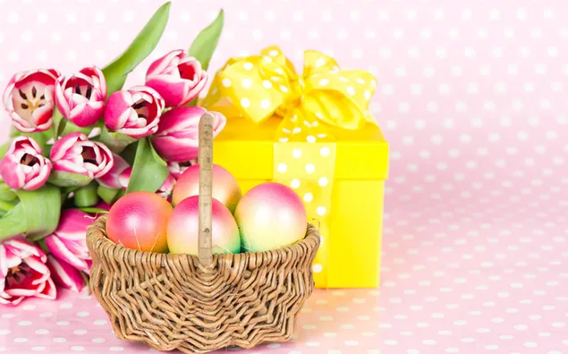 Telur Paskah dalam keranjang dengan tulip merah muda dan kotak hadiah kuning