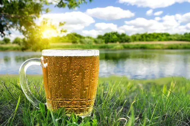 Ein Glas kaltes Bier am Fluss mit Sonnenschein und Himmelshintergrund