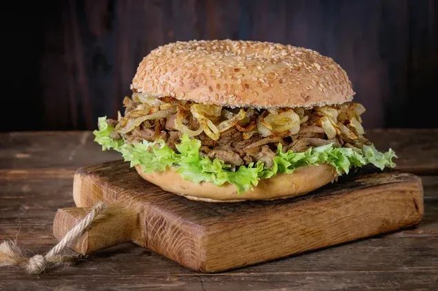 Ein großer Burger mit gesüßten Zwiebeln, Rindfleischpastetchen und Salat in einem Holztablett