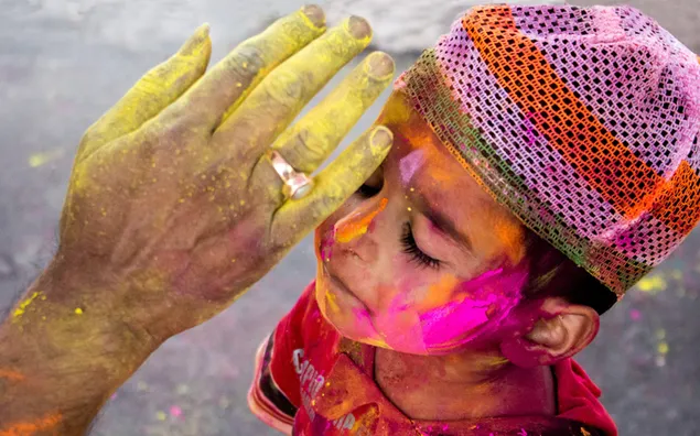 Ein Junge mit Holi-Pulver-Gesicht und der Hand eines älteren Mannes will sein Gesicht streicheln