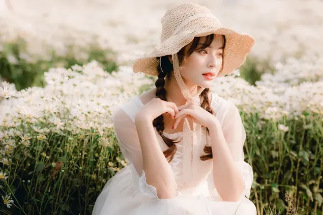 Encantadora chica asiática con su vestido blanco y sombrero de paja en un jardín lleno de flores blancas descargar