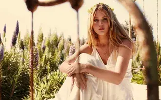 Očarljiva Jennifer Lawrence v beli obleki in cvetlični kroni 2K ozadje