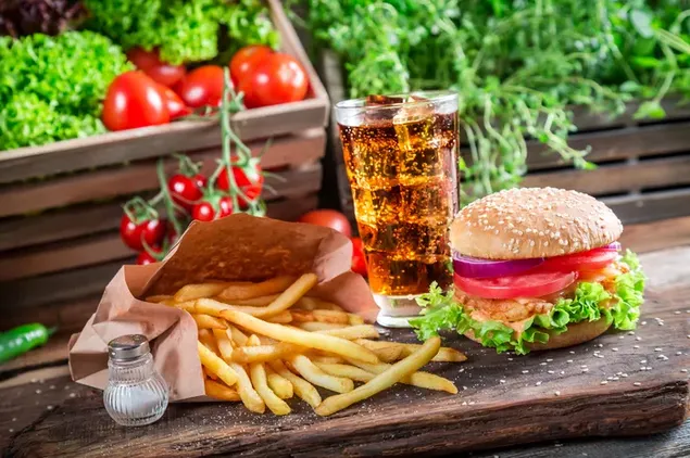 Fast Food - Hamburger und Pommes mit Eistee, Gemüsehintergrund