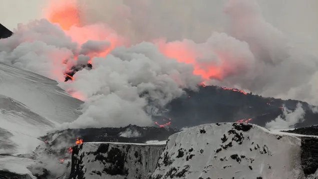 Feuer und Nebel, die vom Vulkan in schneebedeckten Bergen aufsteigen