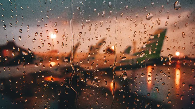 Foto van vliegtuigen op de luchthaven door het raam met opgehoopte regendruppels