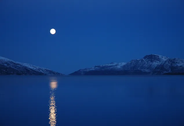 Vista de luna llena de montañas nevadas y lago por la noche