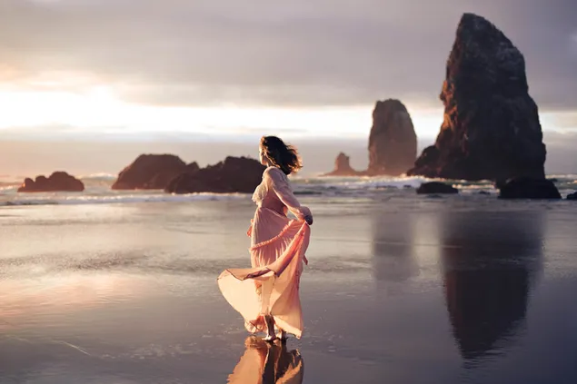 Chica bailando junto a la orilla con formación rocosa y fondo de puesta de sol descargar