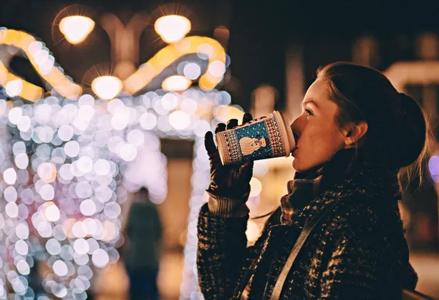 Gadis minum kopi dengan latar belakang lampu Natal