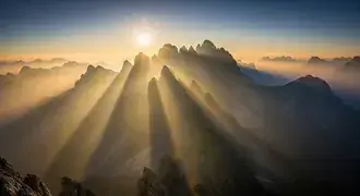 golden sunlight breaks through the mist, casting dramatic rays across towering mountain peaks and creating a breathtaking view of nature's grandeur.
