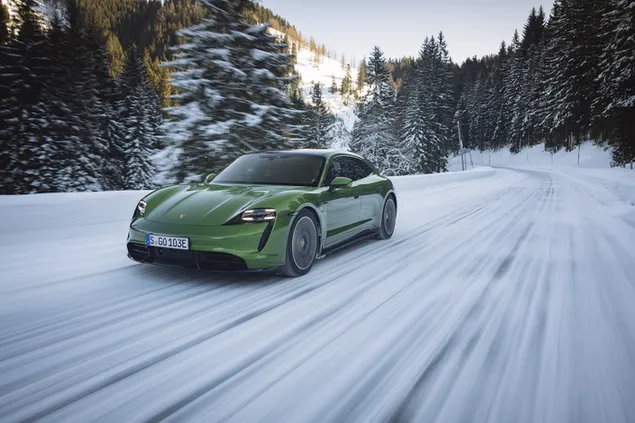Verde porsche taycan turbo S (2022) acelerando a lo largo de un camino forestal nevado