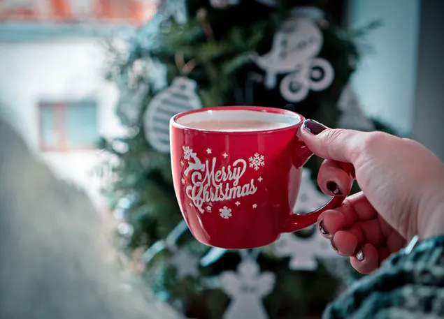 Manos sosteniendo una taza roja de café con saludos de "Feliz Navidad"