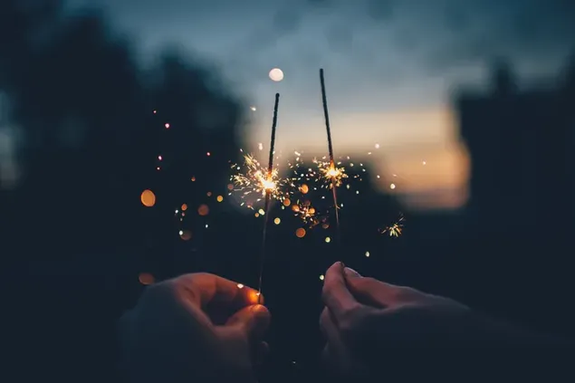 Tangan memegang suar perayaan kecil untuk perayaan tahun baru di depan latar belakang kabur malam