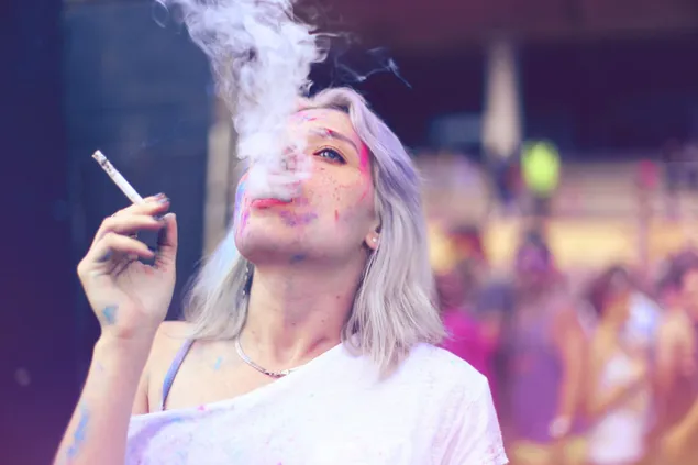 Hermosa mujer fumando cigarrillos y pintura del festival holi en su cara.