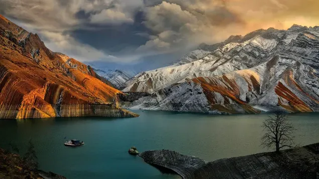 Hermosa vista de botes pequeños, montañas nevadas y cielo nublado oscuro en el lago descargar