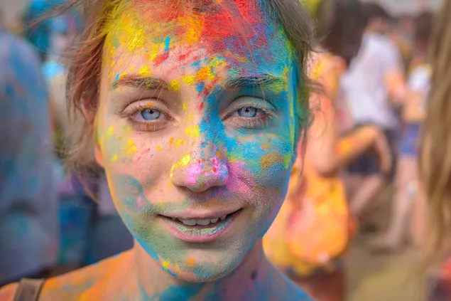 Holi-farver er over hele ansigtet på en pige med blå øjne 2K tapet