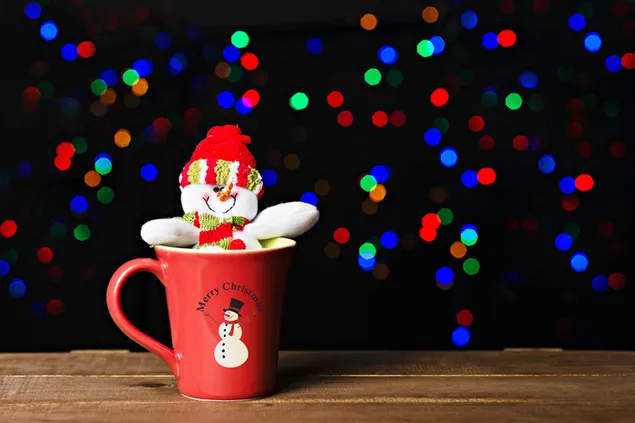 Hombre de nieve sentado en una taza roja con fondo de luces de Navidad de colores