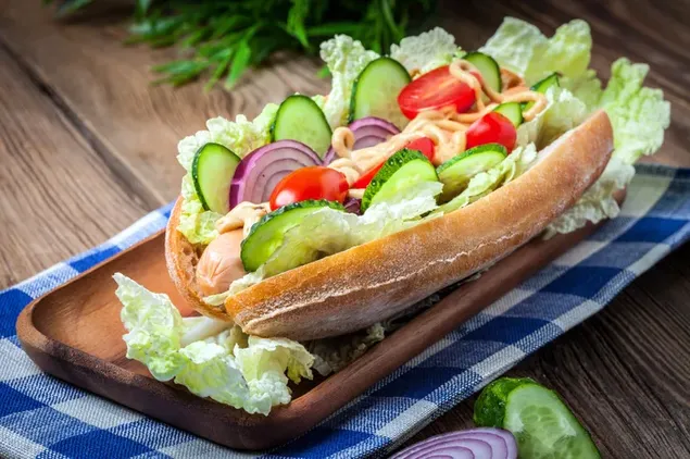 Sándwich de perrito caliente sobrecargado con verduras en bandeja de madera y mantel azul 4K fondo de pantalla