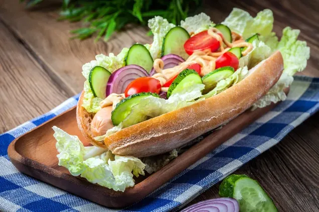 Sandwich hotdog diisi dengan sayuran di nampan kayu dan taplak meja biru