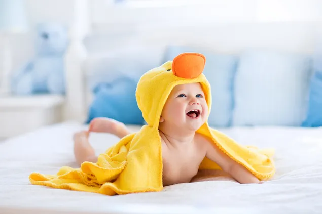 黄色いアヒルの衣装でベッドで幸せに動く赤ちゃんの写真