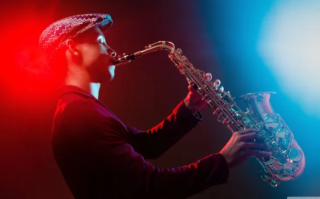 sapkali ve ceketli bir muzisyenin renkli isiklar altinda saksafon esliginde caz performansi indir