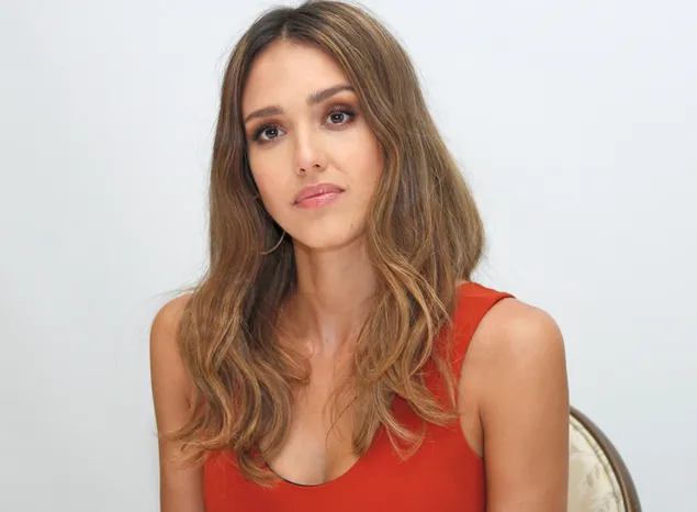 Jessica Alba está sentada en una silla con un vestido rojo frente a una pared blanca 2K fondo de pantalla