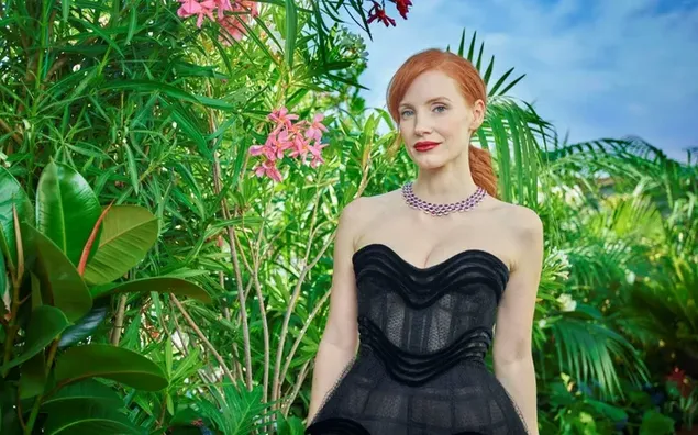 ジェシカ・チャステイン・ジンジャーの女優は、緑の植物を背景にした黒のフィットしたセクシーなドレスを着ています 4K 壁紙