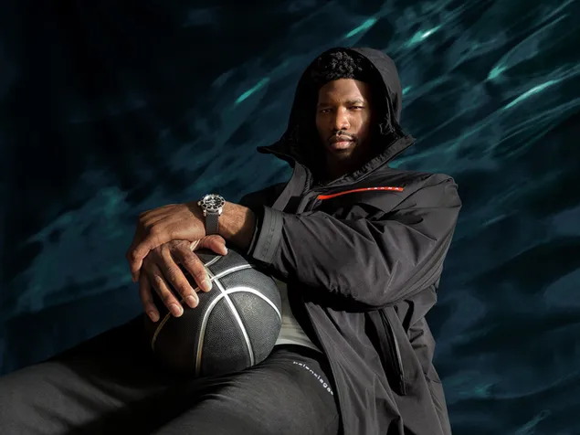 Joel embiid in his black coat, with a black basketball in his hands