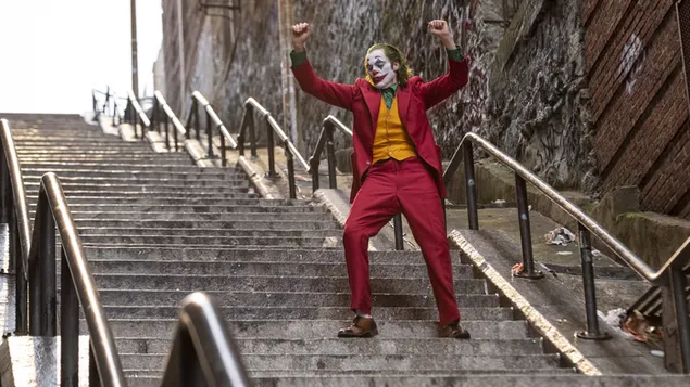 Joker avec son maquillage unique dans une veste rouge et un gilet jaune dans les escaliers à côté des murs peints en graffitis 4K fond d'écran