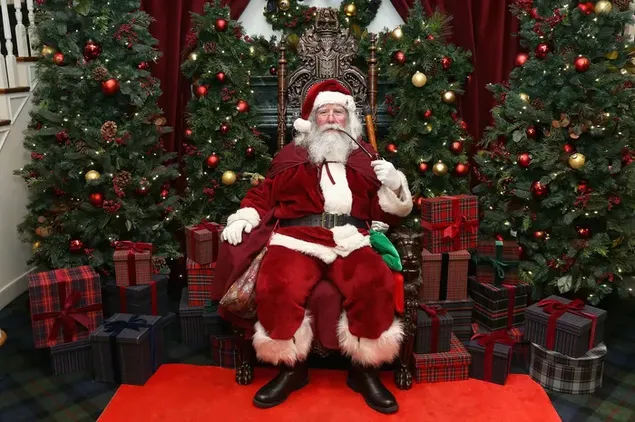 Jolly Santa Claus zittend in zijn stoel met zijn geschenken en kerstboom erachter