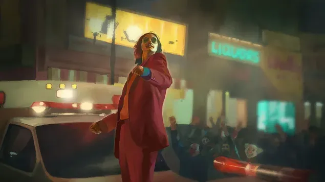 Karakter film Joker berbaju merah menari di jalan di depan mobil dan lampu gedung unduhan
