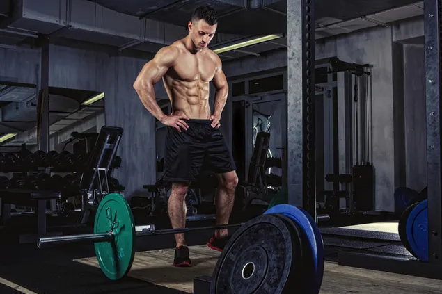 Knappe man bodybuilder poseert met zijn spieren voordat hij gewichten opheft download