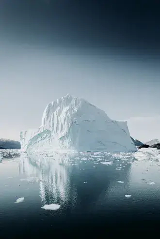 large white iceberg floating in cold blue arctic waters with clear sky above download