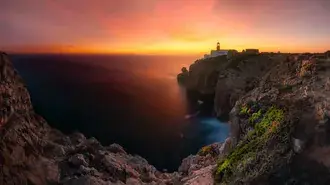 faro sulle scogliere a guardia del tramonto scarica
