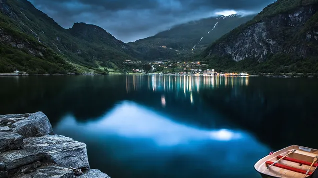 Lights of small town houses surrounded by high misty mountains reflect on lake water