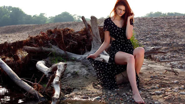 Taustakuva Yksinäinen kaunis nainen, jolla on punaiset hiukset mustassa mekossa istumassa puiden vieressä 2K