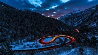 Tapeta Dlouhá expozice fotografie světel aut na asfaltové silnici mezi zasněženými horami a lesem 4K