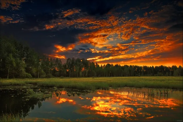 夕焼けのように赤く反射する雲空と湖水に映る木々の壮大な写真