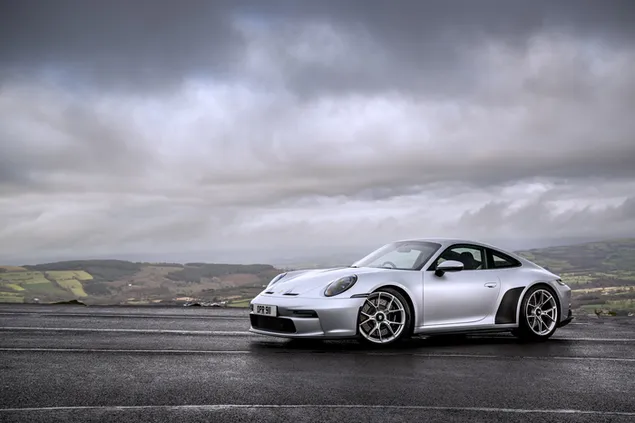 Majestic single-door sports car Porsche with metal-coloured steel wheels on an asphalt road at the edge of misty mountains
